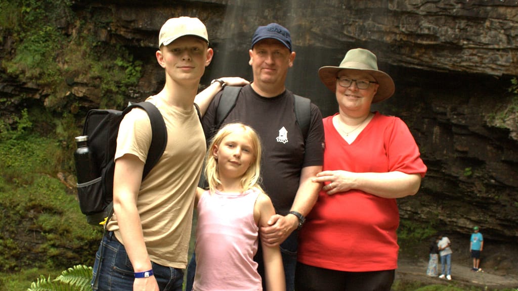 Dansk familie på campingtur foran klippevæg, smilende og klar til eventyr — perfekt til friluftsliv og rejseindhold.