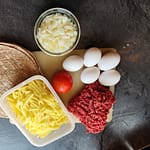 Ingredienser til morgenmadsburrito: hakket oksekød, æg, ost, løg, kartofler og tortilla til campingmad