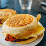 Hjemmebagte engelske breakfast muffins flækket og let ristede, klar til at blive fyldt med æg, bacon og ost.